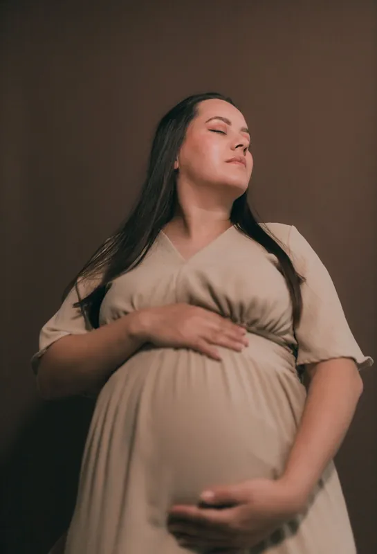 Schwangere Frau im beigen Kleid, Hände am Bauch
