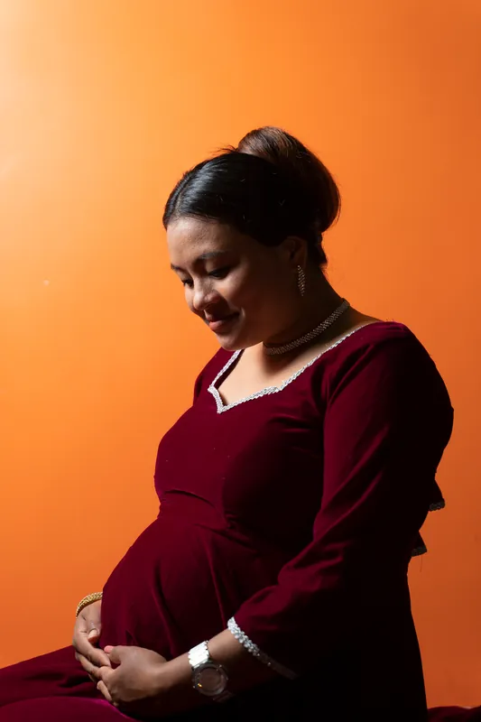 Schwangere Frau im weinroten Kleid vor orangem Hintergrund