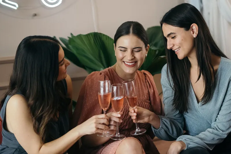 Drei Freundinnen stoßen lachend mit Sekt an