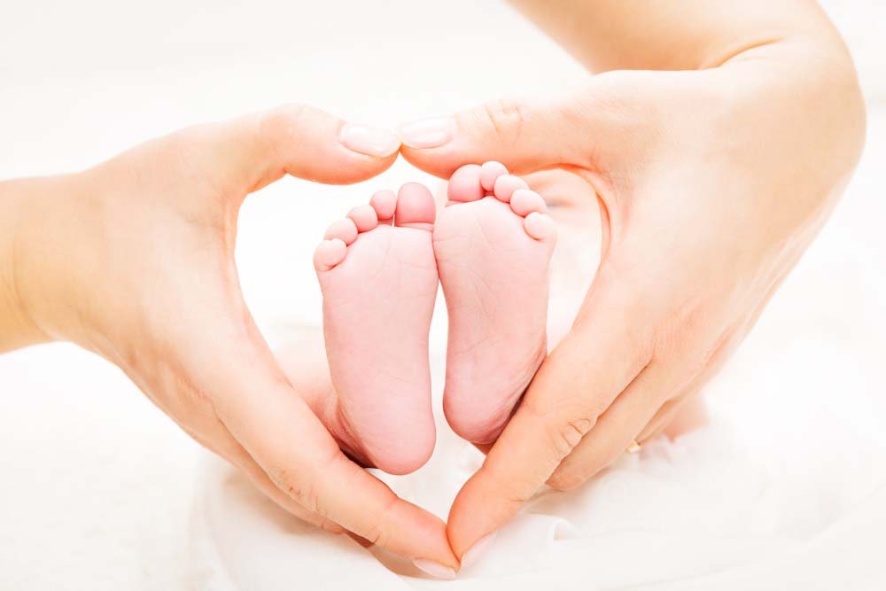 Ein Newborn Foto auf dem die Mutter mit den Händen ein Herz um die Füße des Babys formt